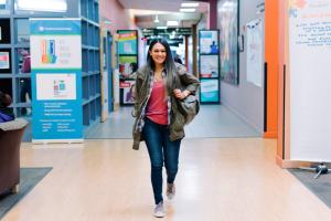 A student walks across a campus hallway smiling