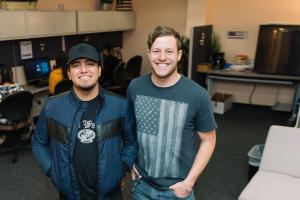 Two veteran students stand smiling in the Veteran Service Center