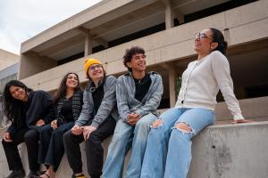 5 students sit on a pony wall in a west campus courtyard